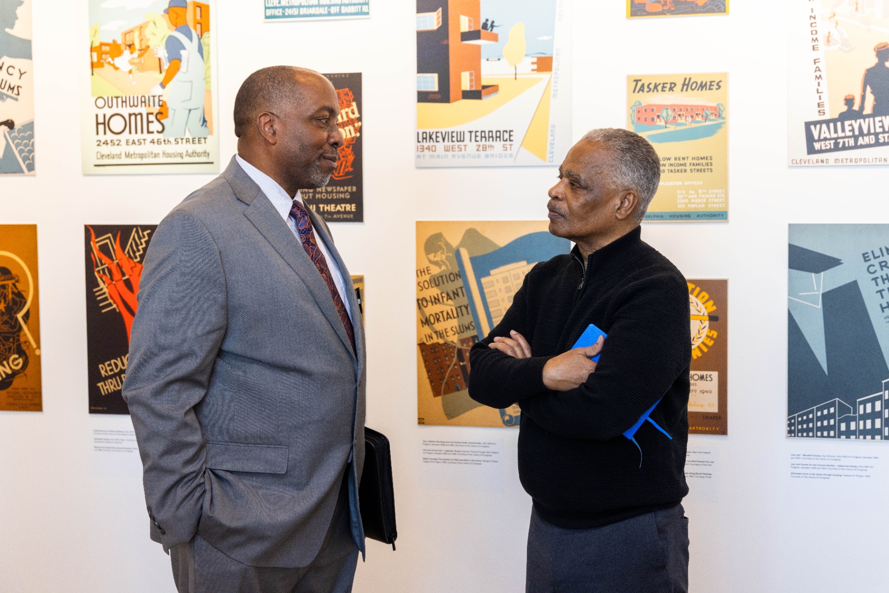 Two leaders in conversation in front of historic housing posters